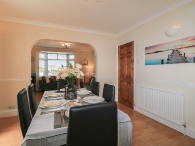 A dining room with a set table and black chairs next to a living room with a sofa and a large window at Hilltop Cottage in Paignton
