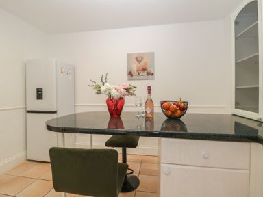 A kitchen with a refrigerator a countertop with a flower vase a bottle of prosecco two glasses and a fruit basket in Hilltop Cottage Paignton