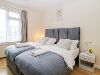 A bedroom with two single beds pushed together with blue bedding and a bedside table with a lamp and flowers at Hilltop Cottage in Paignton