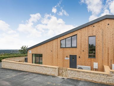 Exterior view of a wooden building with stone wall and gate at Bears Court Barn 1 in Little Rissington near Bourton-On-The-Water