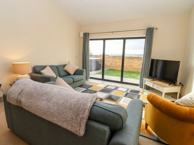 A living room with sofas a TV on a stand and sliding glass doors at Bears Court Barn 1 Little Rissington near Bourton-On-The-Water
