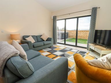 A living room with sofas a lamp rug and TV with sliding glass door at Bears Court Barn 1 Little Rissington near Bourton-On-The-Water