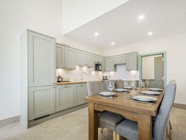 A kitchen with green cabinets and a wooden dining table set with plates and glasses at Bears Court Barn 1 in Little Rissington near Bourton-On-The-Water