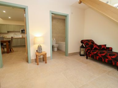 A hallway with a wooden side table and lamp between two doors near a chaise lounge and a kitchen at Bears Court Barn 1 Little Rissington near Bourton-On-The-Water