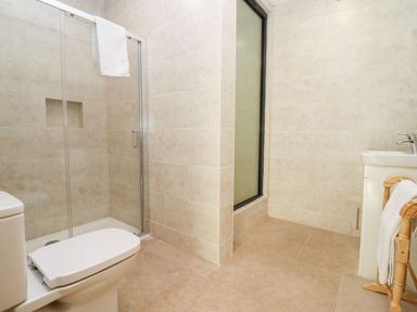 A bathroom with a toilet, shower area with glass door, sink with faucet, towel rack with towels at Bears Court Barn 1 Little Rissington near Bourton-On-The-Water
