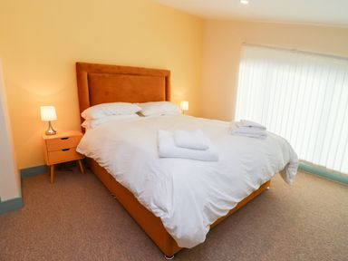 A bedroom with a bed with white bedding two bedside tables with lamps and folded towels on the bed at Bears Court Barn 1 in Little Rissington near Bourton-On-The-Water