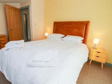 A bedroom with a large bed with white bedding and towels on top a brown headboard two bedside tables with lamps a wooden door a chest of drawers at Bears Court Barn 1 Little Rissington near Bourton-On-The-Water