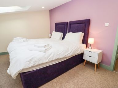A bedroom with a double bed white bedding purple headboard bedside table with lamp at Bears Court Barn 1 Little Rissington near Bourton-On-The-Water