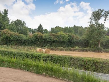 A field with two hay bales behind a hedge and trees at Bears Court Barn 1 in Little Rissington near Bourton-On-The-Water