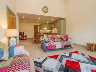 A seating area with patchwork sofas and a geometric rug near a kitchen and dining table at Bears Court Barn 2 in Little Rissington near Bourton-On-The-Water
