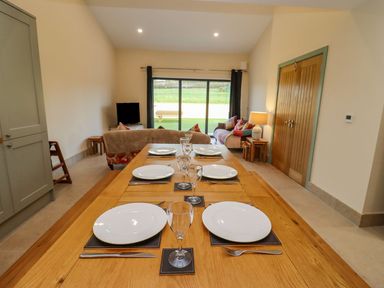 A dining table set with plates and glasses in a room with a sofa TV and sliding glass doors at Bears Court Barn 2 Little Rissington near Bourton-On-The-Water