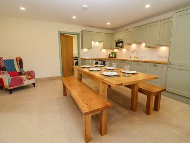 A kitchen with sage green cabinets a wooden table with benches and a patchwork armchair at Bears Court Barn 2 Little Rissington near Bourton-On-The-Water
