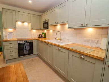 A kitchen with green cabinets wooden countertop white sink and built in oven at Bears Court Barn 2 Little Rissington near Bourton-On-The-Water