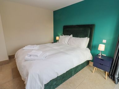A bedroom with a double bed with white bedding bedside tables with lamps and folded towels on the bed at Bears Court Barn 2 Little Rissington near Bourton-On-The-Water