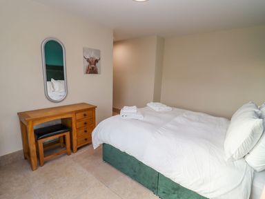 A bedroom with a bed covered in white bedding and towels on top a wooden desk with drawers and a bench and a mirror on the wall at Bears Court Barn 2 in Little Rissington near Bourton-On-The-Water