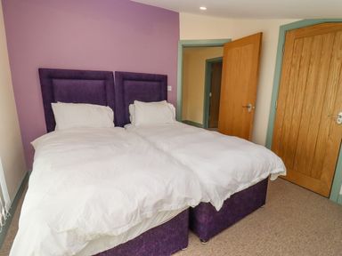 A bedroom with two single beds with white bedding and purple headboards by a purple wall at Bears Court Barn 2 in Little Rissington near Bourton-On-The-Water