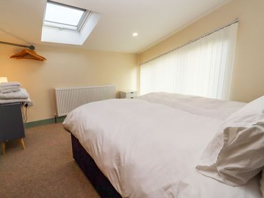A bedroom with a bed white bedding a skylight window radiator towels on a side table and hangers on a rail at Bears Court Barn 2 in Little Rissington near Bourton-On-The-Water