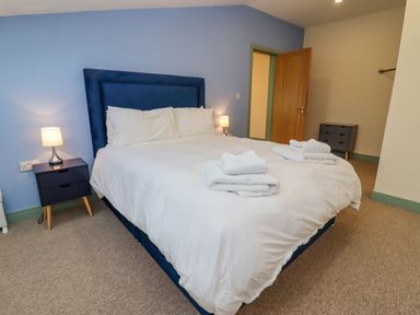 A bedroom with a bed with white linens and towels on top and bedside tables with lamps at Bears Court Barn 2 in Little Rissington near Bourton-On-The-Water