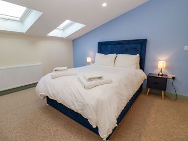 A bedroom with a double bed a blue headboard bedside tables lamps and skylights at Bears Court Barn 2 Little Rissington near Bourton-On-The-Water