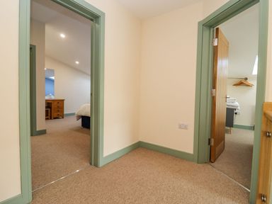 A hallway with two open doorways showing a bedroom and a room with folded towels at Bears Court Barn 2 Little Rissington near Bourton-On-The-Water