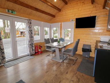 A dining area with a table and four chairs next to windows and a wall-mounted TV at Drumrane Lodge in Dungiven Londonderry