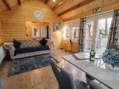A wooden living room with a sofa a rug a table with chairs and a bottle at Drumrane Lodge in Dungiven Londonderry