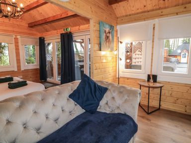 A wooden cabin interior with a tufted sofa a bed with folded towels curtains and a side table with a lamp at Drumrane Lodge Dungiven Londonderry