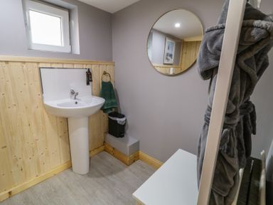A bathroom with a pedestal sink green towel trash bin round mirror and a gray bathrobe hanging at Drumrane Lodge in Dungiven Londonderry