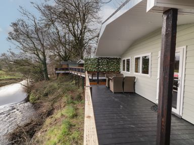A wooden deck with outdoor chairs beside a river at Railway Lodge in Dungiven Londonderry