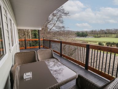 A balcony with wicker chairs and a table overlooking fields and trees at Railway Lodge in Dungiven Londonderry