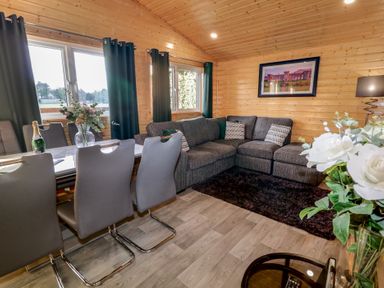 A wooden living room with a grey corner sofa white dining table and grey chairs at Railway Lodge in Dungiven Londonderry