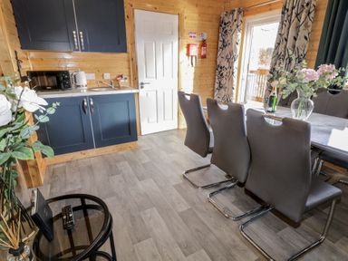 A dining area with gray chairs around a marble table next to a kitchenette with blue cabinets and wooden walls at Railway Lodge in Dungiven Londonderry