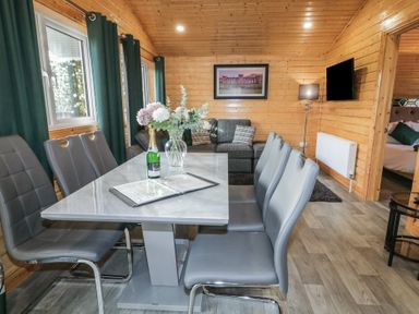 A dining area with a table and chairs next to a living room with a sofa and a television at Railway Lodge in Dungiven Londonderry
