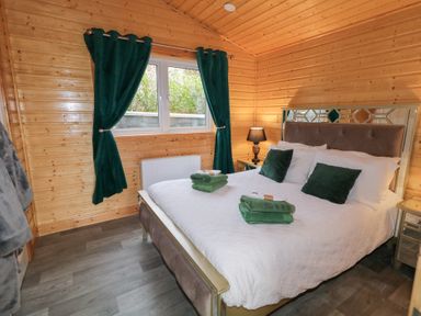 A bedroom with a large bed green cushions and towels bedside table with lamp and green curtains at Railway Lodge in Dungiven Londonderry