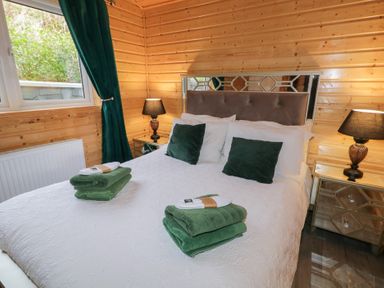 A bedroom with a bed with white bedding green pillows and green towels with slippers on top at Railway Lodge in Dungiven Londonderry