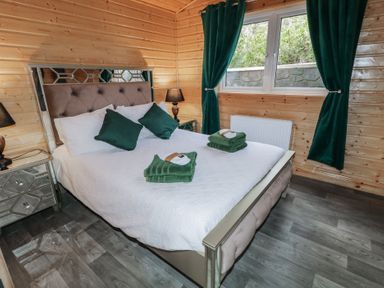 A bedroom with a bed with white bedding green pillows and towels wooden walls and floor at Railway Lodge in Dungiven Londonderry