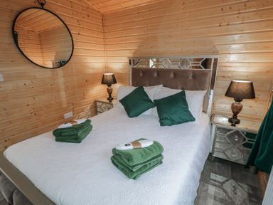 A bedroom with a bed with green pillows two nightstands with lamps and wooden walls at Railway Lodge in Dungiven Londonderry