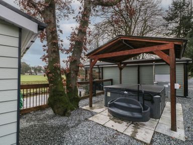 An outdoor area with a hot tub under a wooden canopy next to trees and a fenced grassy field at Railway Lodge in Dungiven Londonderry