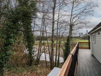 A balcony with wooden railing overlooking trees and a river at Railway Lodge in Dungiven Londonderry
