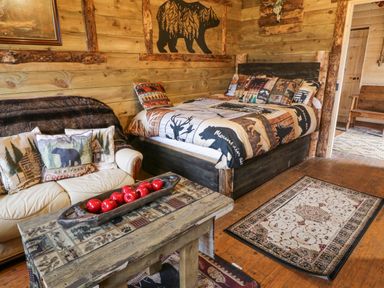 A rustic bedroom with a wooden bed and nature-themed bedding a wooden coffee table with red apples on it a cream sofa with bear and cabin cushions at Bear Claw Lodge in Castlerock