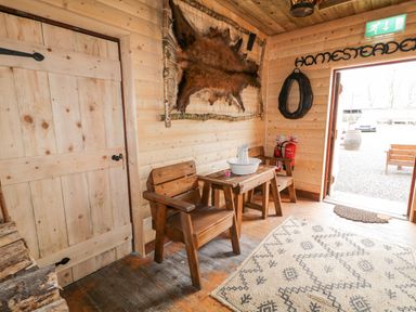 A wooden room with two chairs a small table with a white basin and jug a mounted animal hide and an open door at Bear Claw Lodge in Castlerock