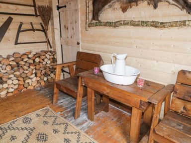 A wooden interior room with stacked firewood a wooden table and chairs a white pitcher in a basin and a broom at Bear Claw Lodge in Castlerock