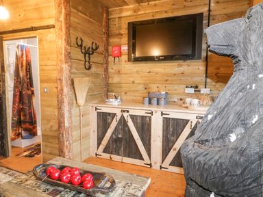A rustic wooden room with a TV mounted on the wall a wooden cabinet with containers a broom and a carved bear statue at Bear Claw Lodge in Castlerock
