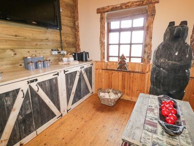 A room with rustic wooden cabinets a large carved bear statue and a table with red decorations at Bear Claw Lodge in Castlerock