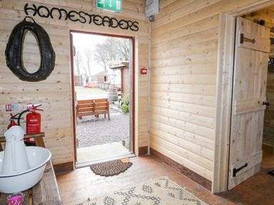 An open wooden door leading outside with a bench visible outside a wooden room with homesteaders sign above the door at Bear Claw Lodge in Castlerock
