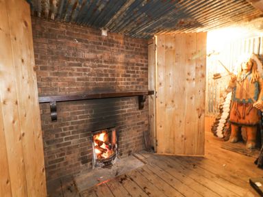 A room with a brick fireplace with a fire burning and wooden walls and floor at Bear Claw Lodge in Castlerock