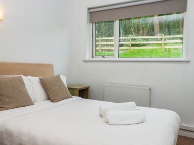 A bedroom with a bed with pillows and towels next to a window showing a fenced garden at Castle View Lodge in Ilfracombe