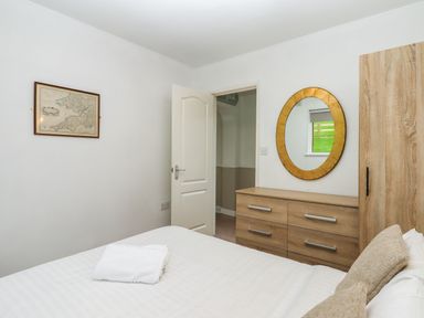 A bedroom with a bed, wooden dresser with an oval mirror, a framed map on the wall and an open door at Castle View Lodge Ilfracombe