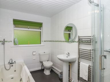 A bathroom with a bathtub toilet sink round mirror heated towel rail and frosted window with green blind at Castle View Lodge in Ilfracombe