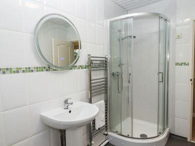 A bathroom with a pedestal sink a circular mirror a glass enclosed shower and a towel rack at Castle View Lodge in Ilfracombe